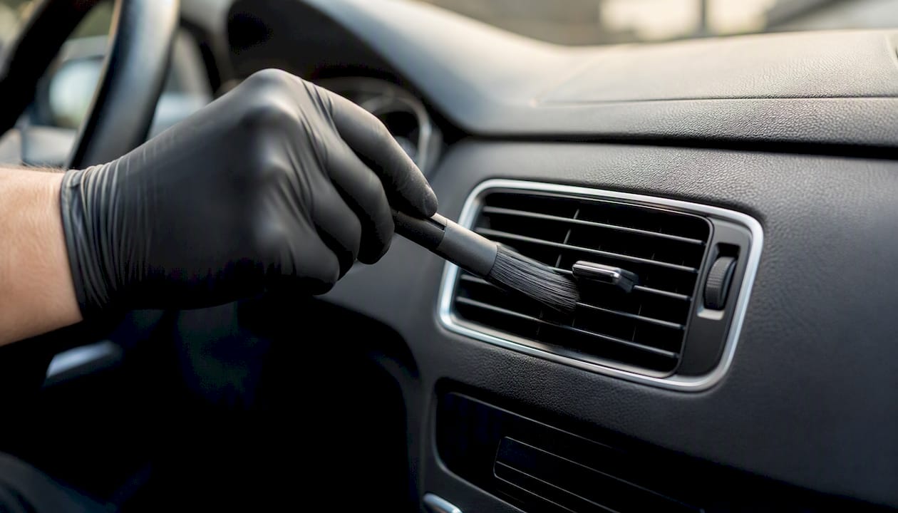 Met de hand de ventilatieroosters van de auto schoonmaken met een borsteltje.