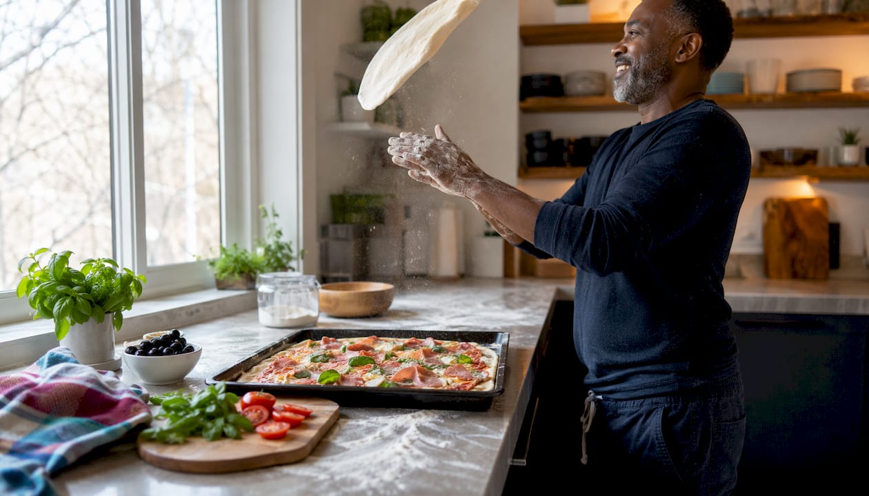 Hands stretching dough beside sheet pan pizza