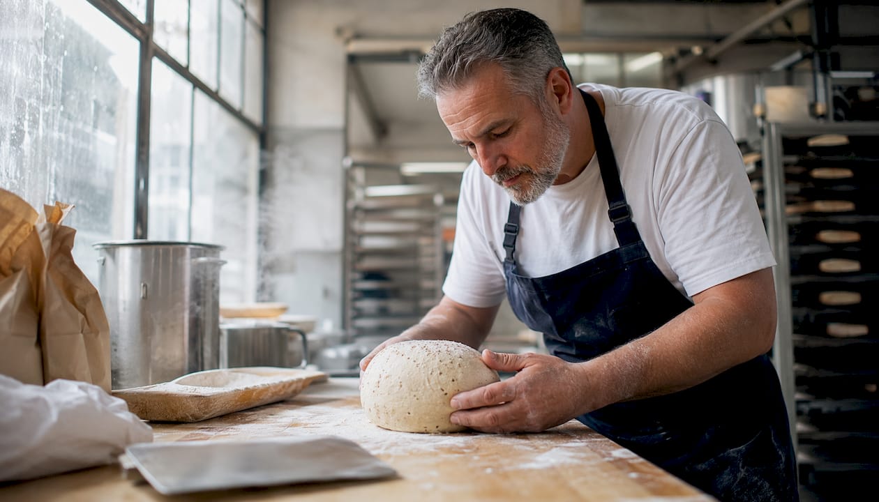 Baker examining cold-fermented pizza dough ball on peel