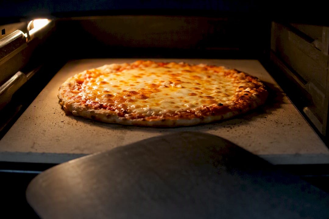 Home pizza oven with pizza on upper rack browning cheese