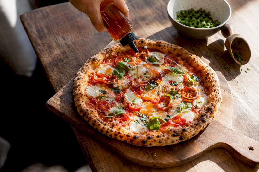 Hand drizzling hot honey from squeeze bottle on pizza