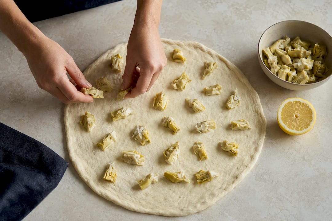 Evenly spaced artichoke pieces on pizza dough