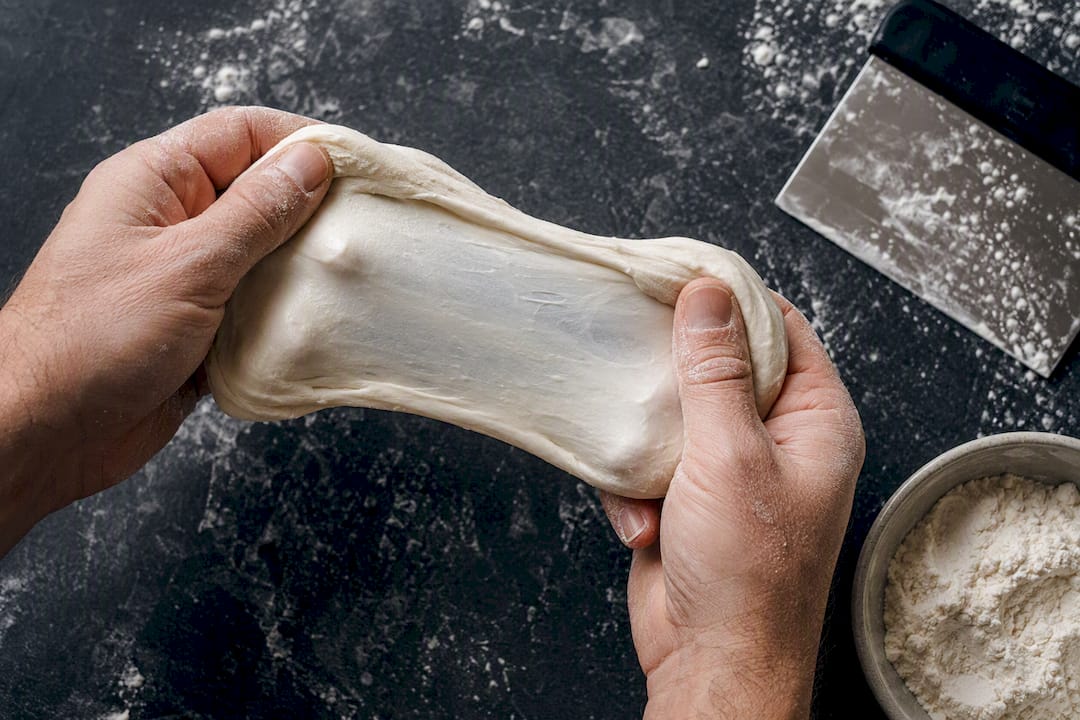 Hands stretching dough into thin gluten membrane