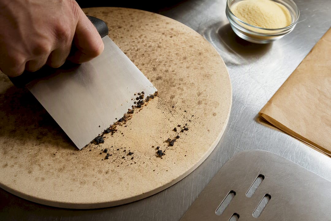Scraper clearing burnt flour from stone