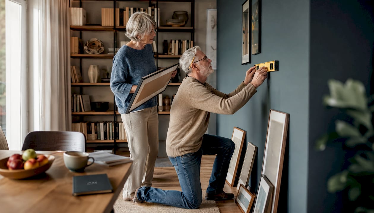 Ein älteres Ehepaar legt Bilder auf dem Boden aus und überlegt, wie sie an der Wand am besten wirken.