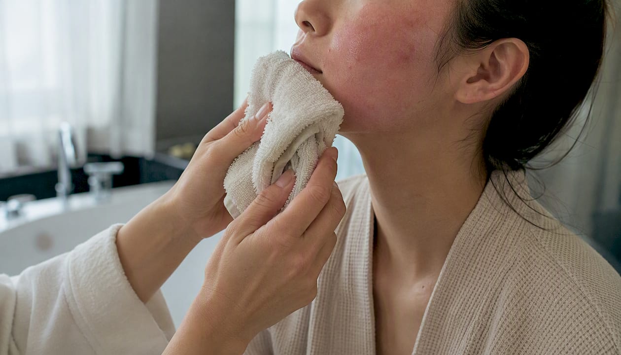 Hands applying cool compress to face