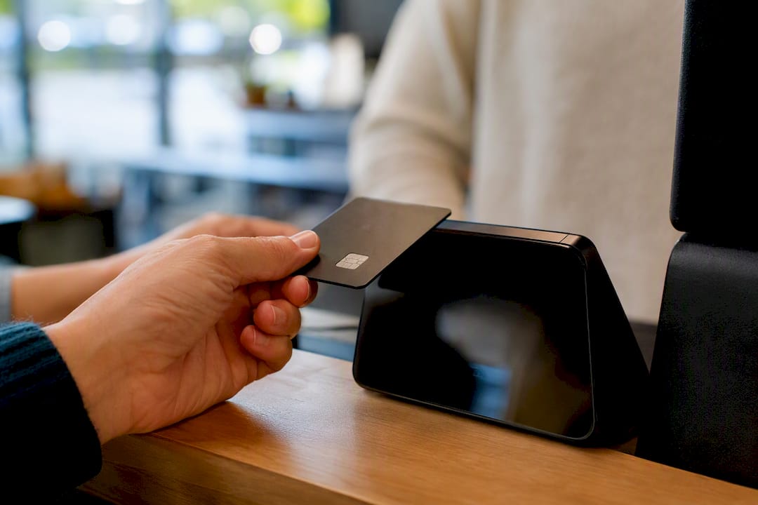 Una mano acerca una tarjeta al datáfono para realizar un pago.