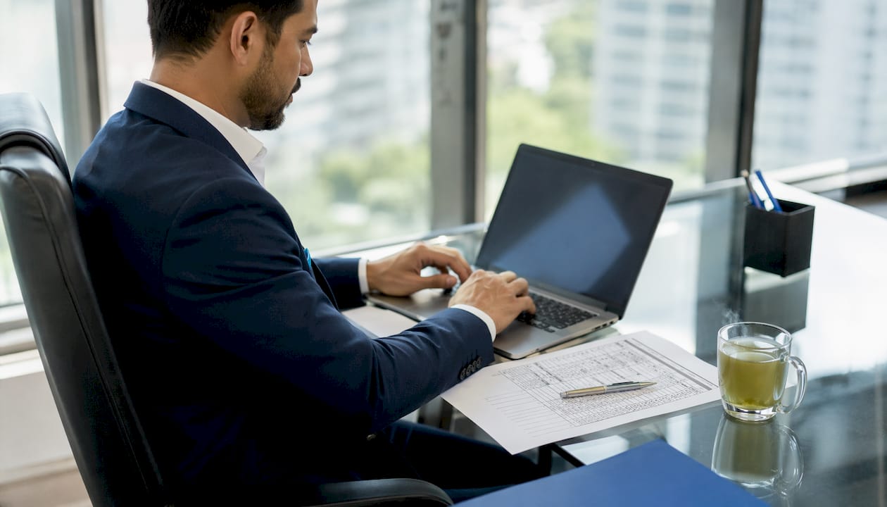 Businessman typing with tender cost documents nearby
