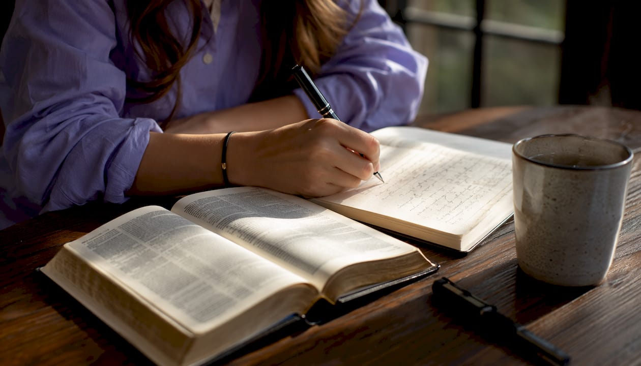 Una mano annota pensieri su un quaderno, con la Bibbia aperta lì vicino.