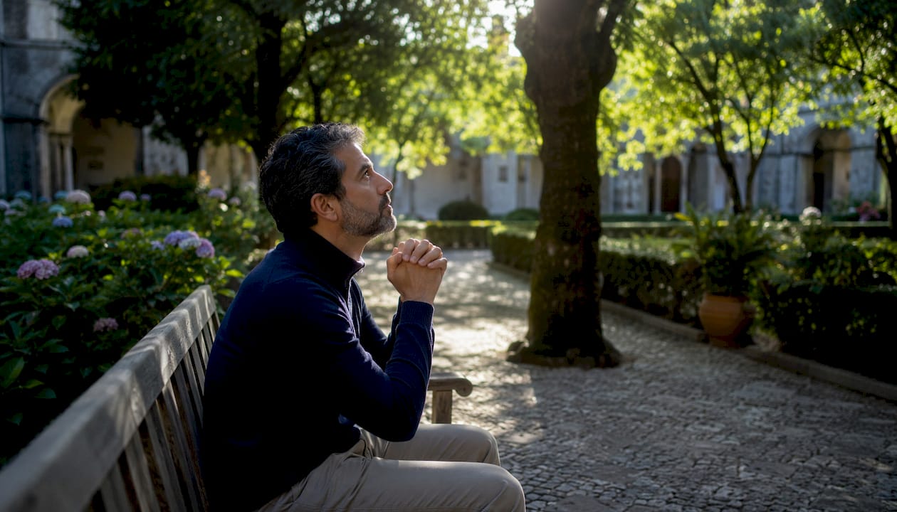 Un uomo raccoglie le mani in preghiera nel suo giardino, mentre il sole scende all’orizzonte e il cielo si tinge di colori caldi.