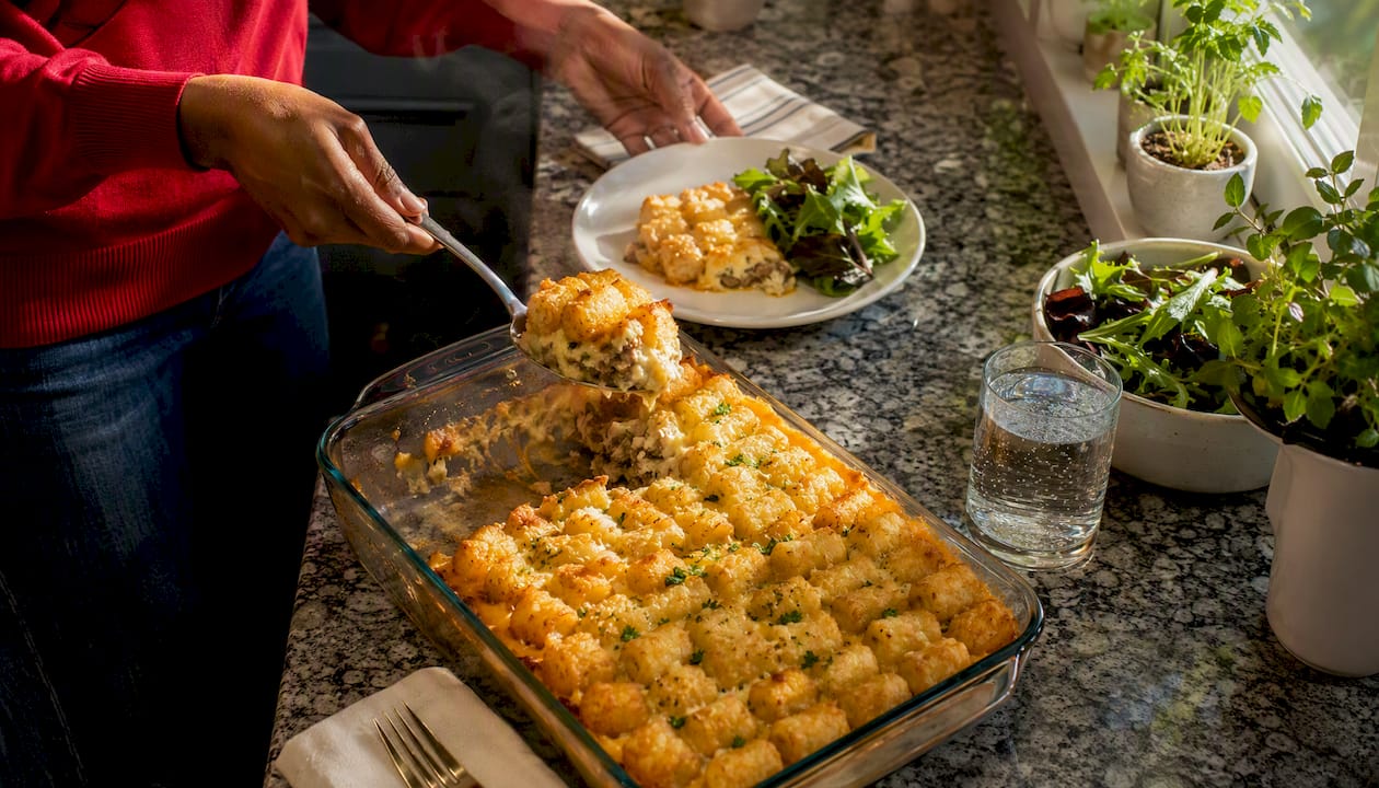 Person serving hot tater tot casserole onto plate