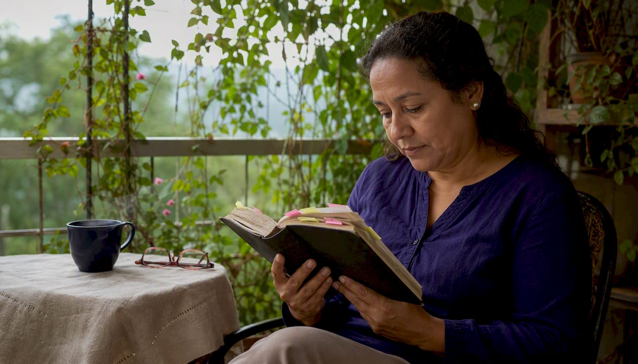 Una mujer sentada a la mesa de la cocina lee pasajes de la Biblia con atención.