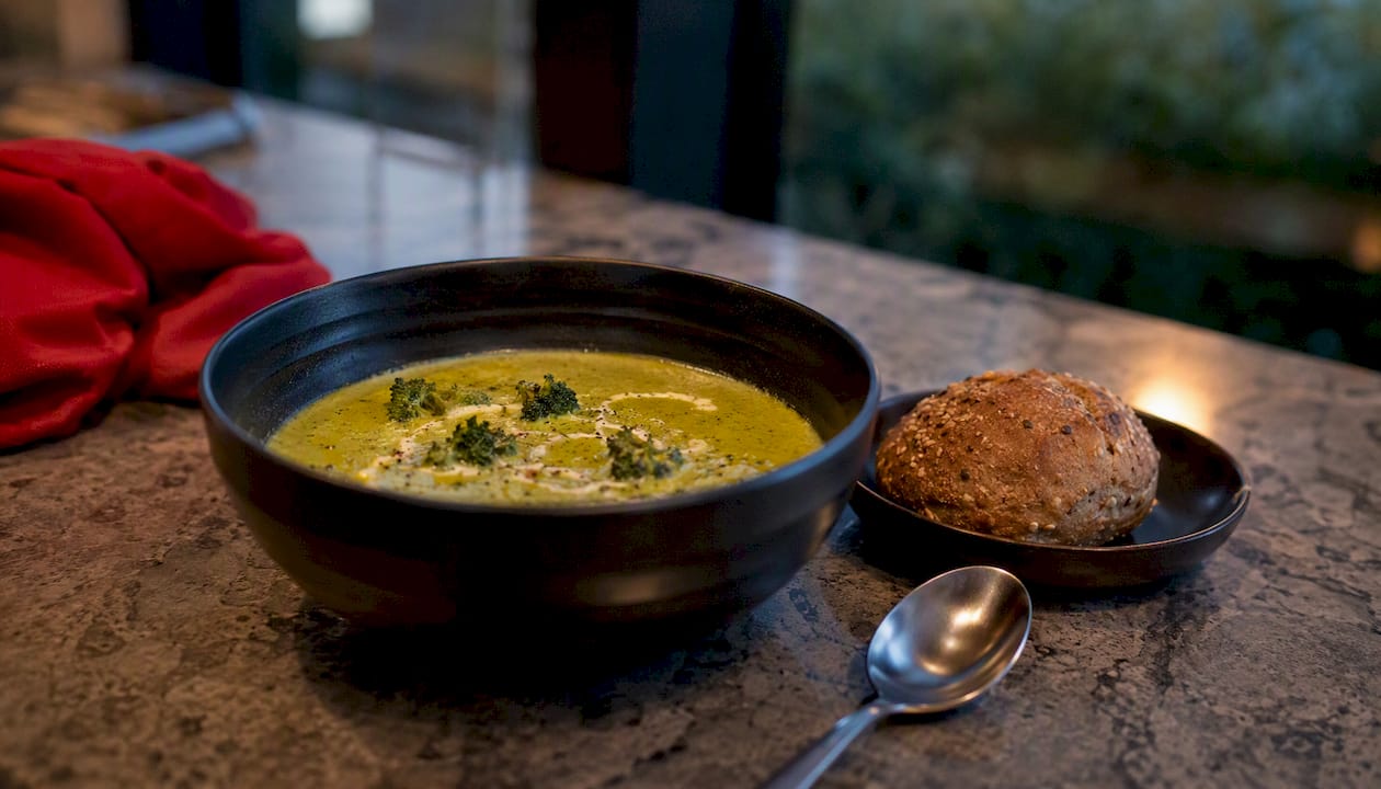 Bowl of bright green broccoli cheddar soup with bread