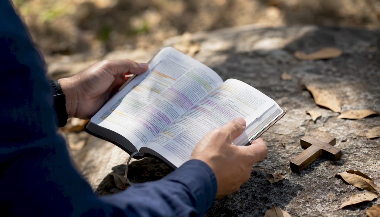 Unas manos sostienen una Biblia abierta, donde se pueden ver varios versículos resaltados.