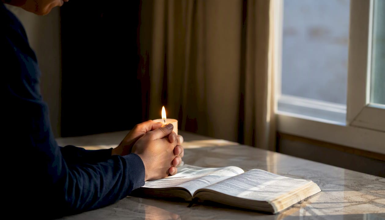 Unas manos sostienen una vela encendida junto a una Biblia.
