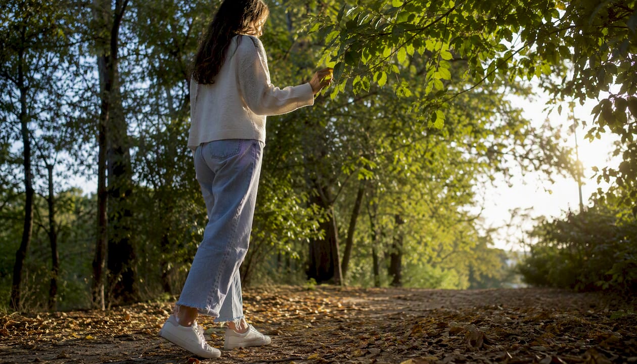 Una mujer camina tranquilamente por un sendero rodeado de árboles.