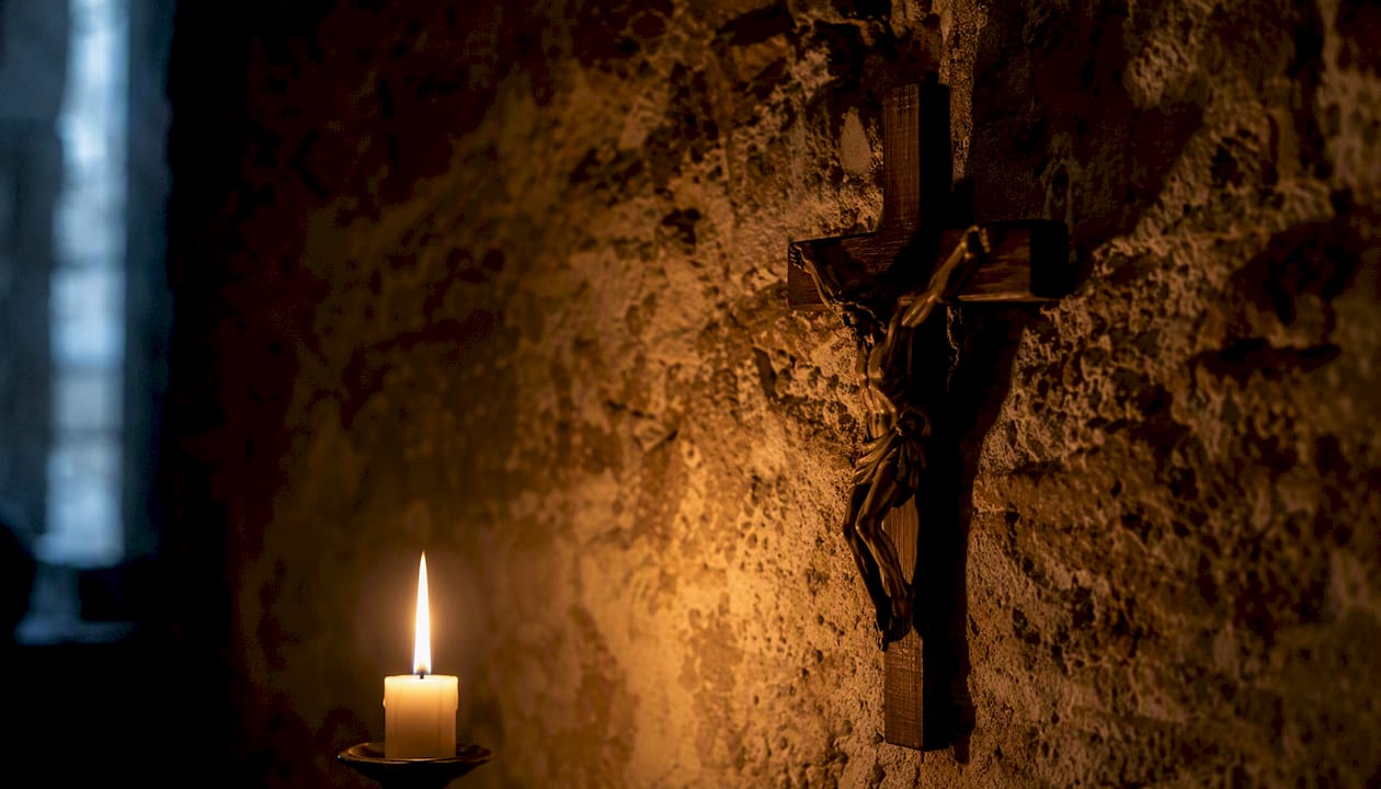 Una croce risplende nella penombra della cappella, illuminata solo dalla tenue luce delle candele.