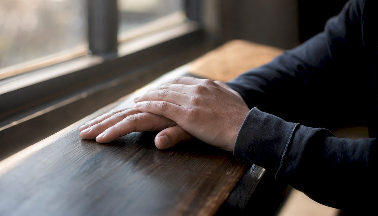Le mani poggiate con delicatezza sulla trave di legno, in un gesto che rivela tutta la loro fragilità.