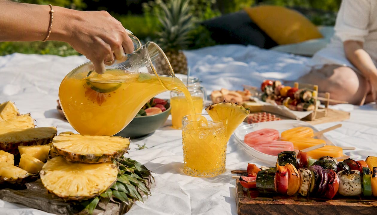 Hand pouring tropical drink over picnic food