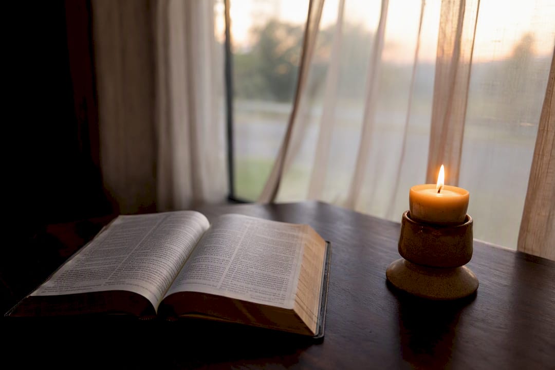 Las páginas abiertas de la Biblia resplandecen suavemente bajo la luz cálida de una vela.