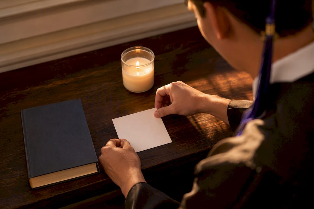 Unas manos colocan una tarjeta con un versículo bíblico junto a una Biblia y una vela encendida.