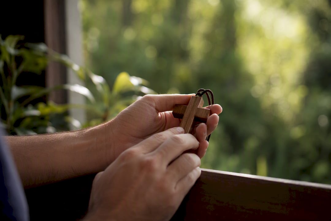 Unas manos sostienen un colgante en forma de cruz de madera.