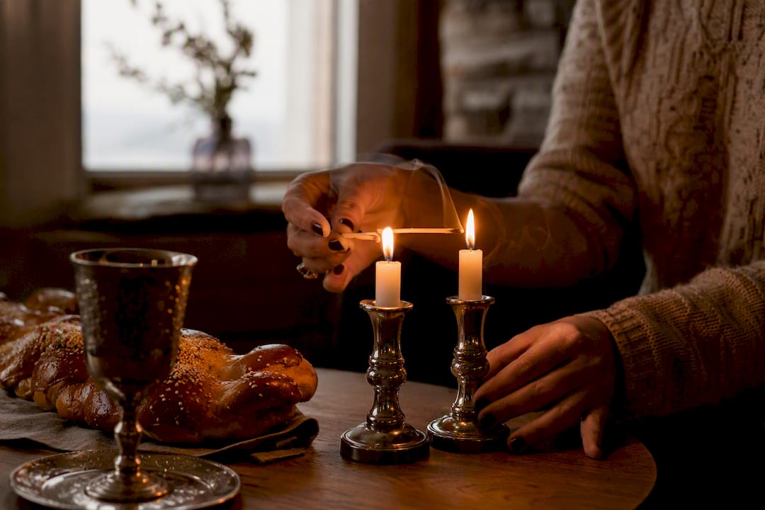 Hands lighting Shabbat candles in warm home setting