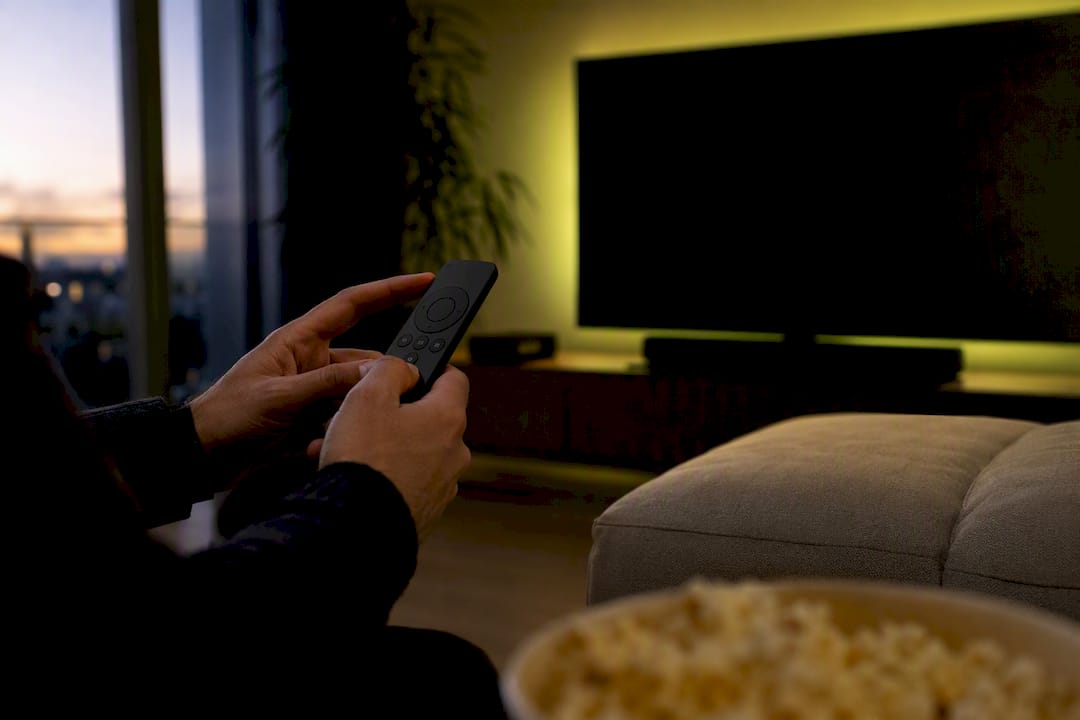 Mani che tengono un telecomando in un salotto domestico dallo stile cinematografico