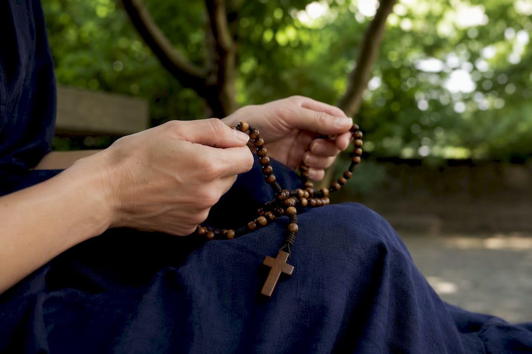 Mani che tengono il rosario in preghiera