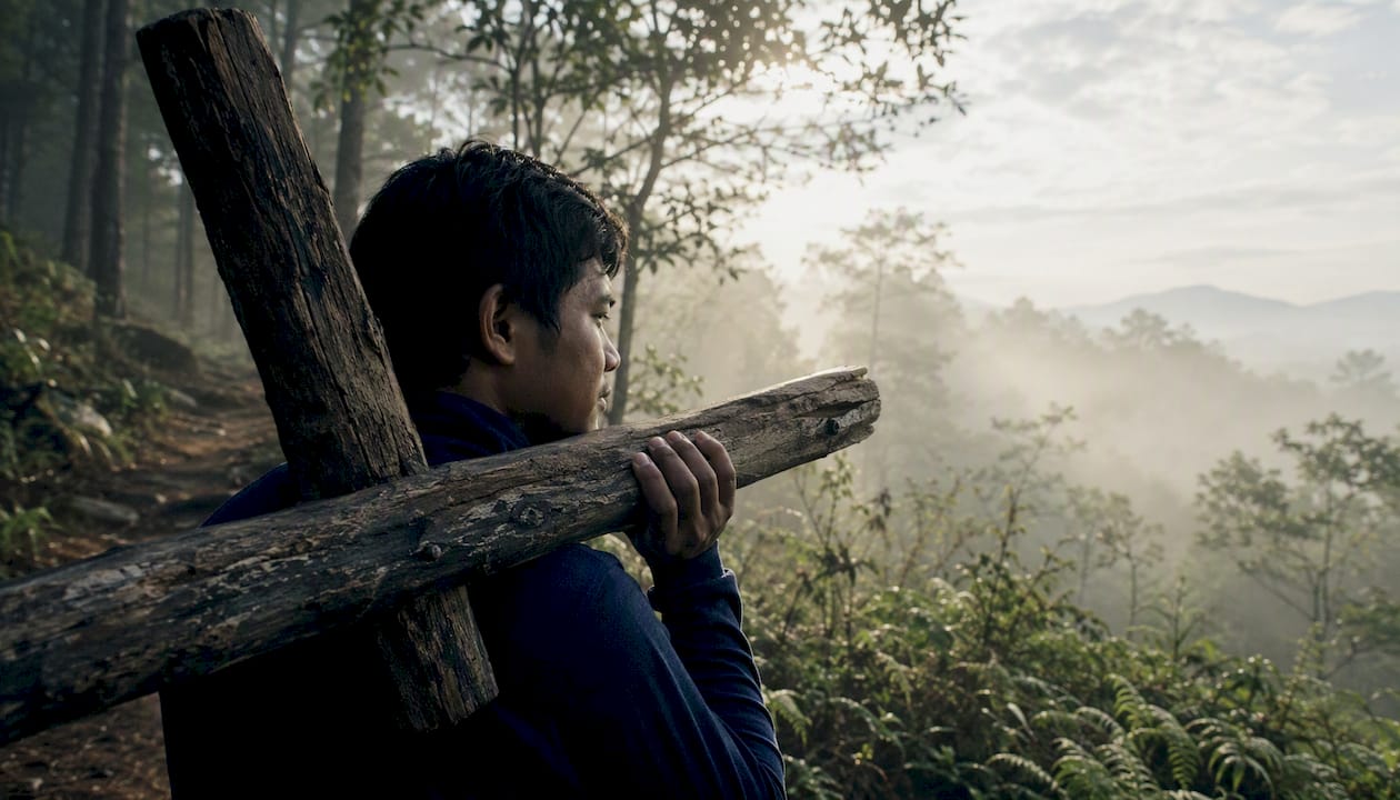 Person carrying wooden cross on path at sunset