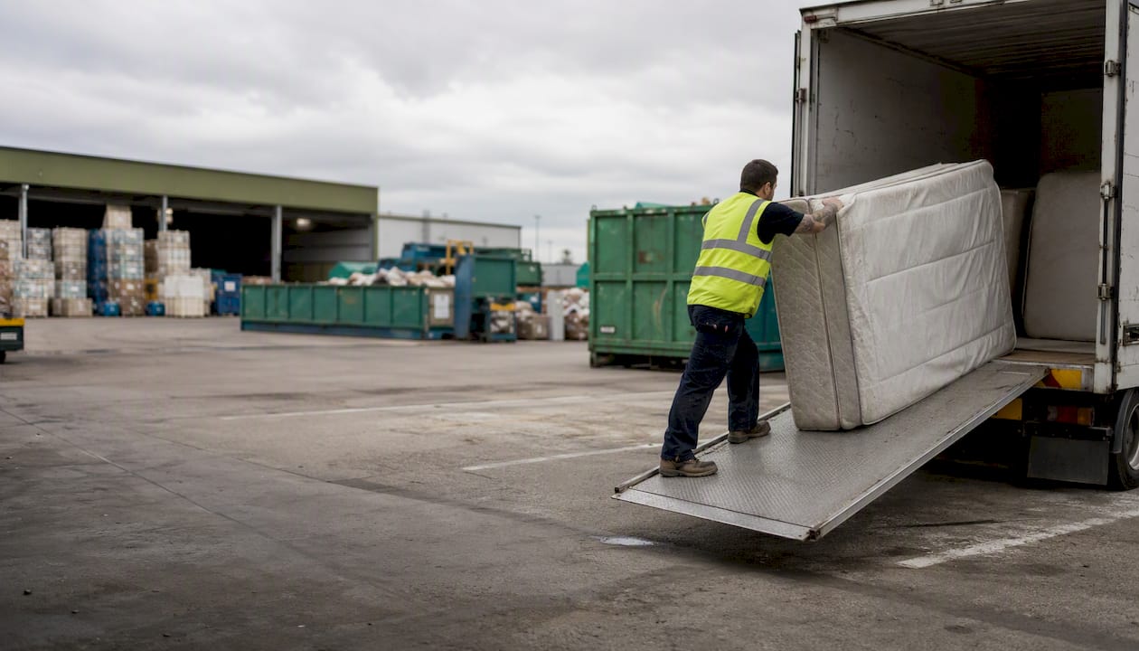 Worker loading mattress at recycling drop-off