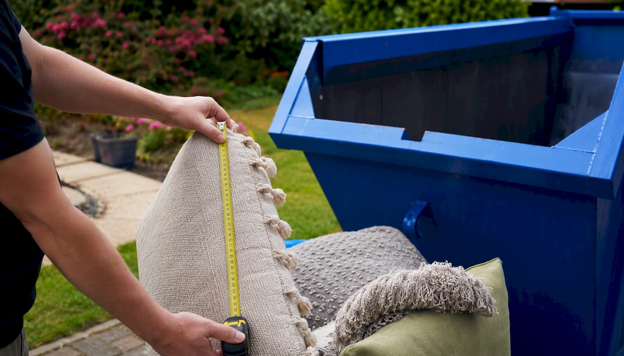Hands placing household items into skip bin