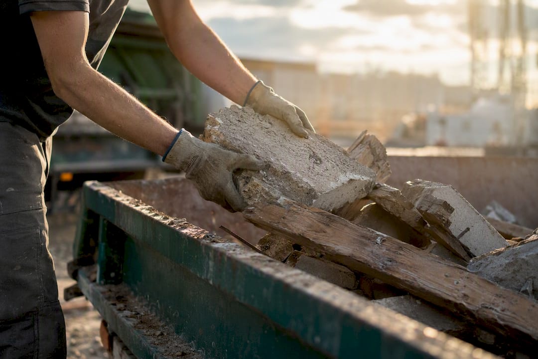 Hands loading skip bin with construction waste