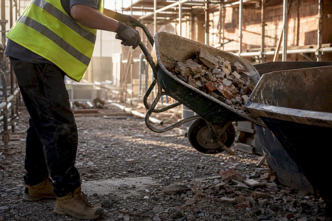 Worker loading demolition debris into skip bin
