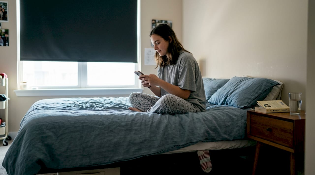 Woman using phone in cozy bedroom with blinds