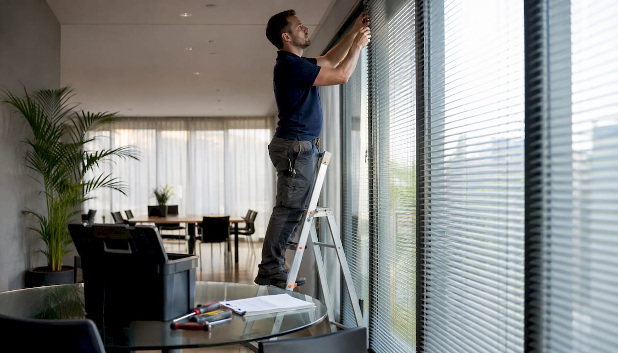 Maintenance worker repairing commercial window blinds