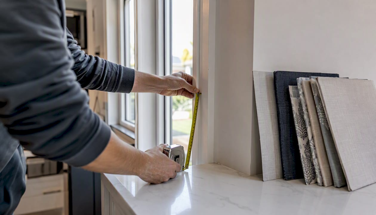 Hands measuring window frame for Roman shades