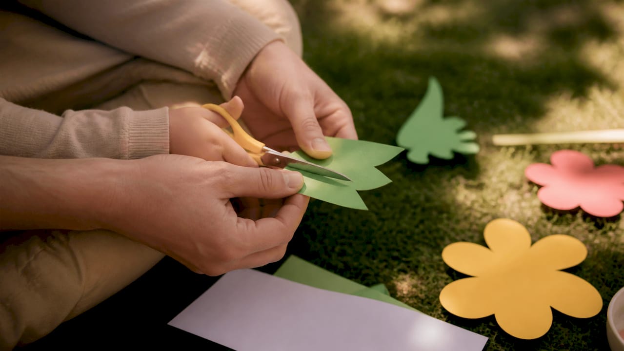 Parent hands guiding toddler's scissor practice