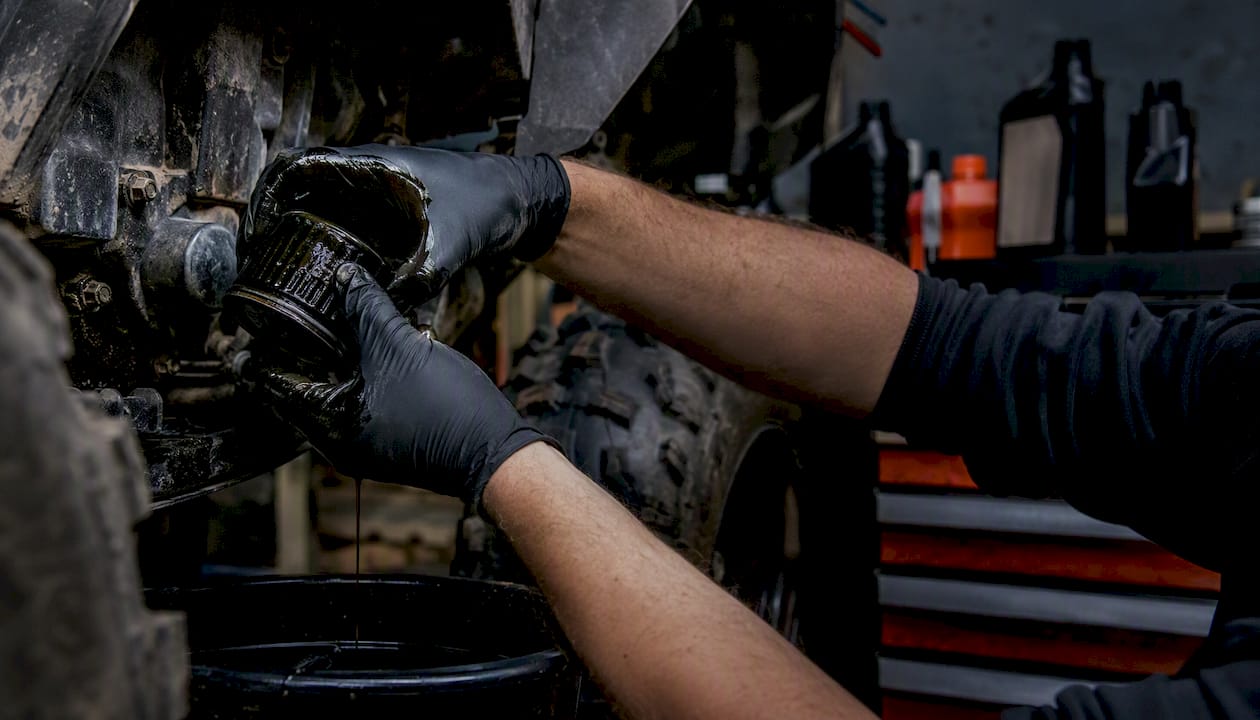Hands draining ATV oil in garage workshop