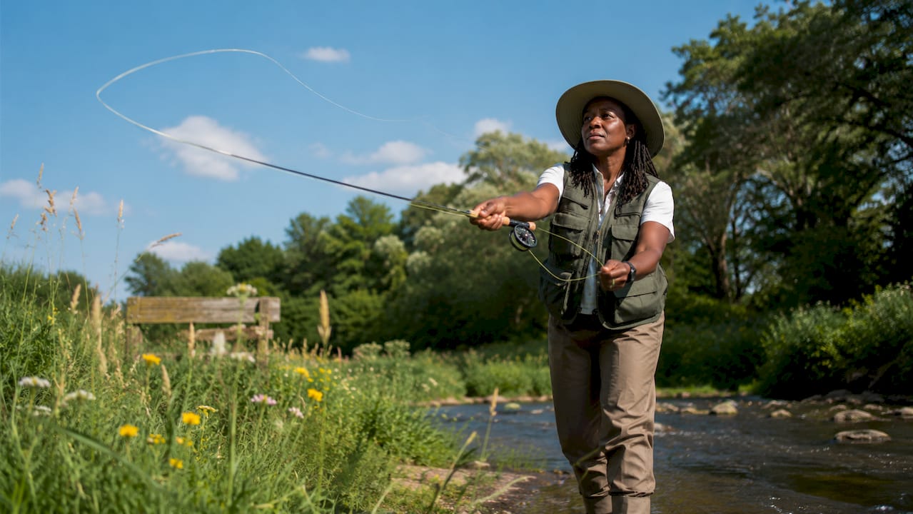 Woman practicing fly casting outdoors by stream