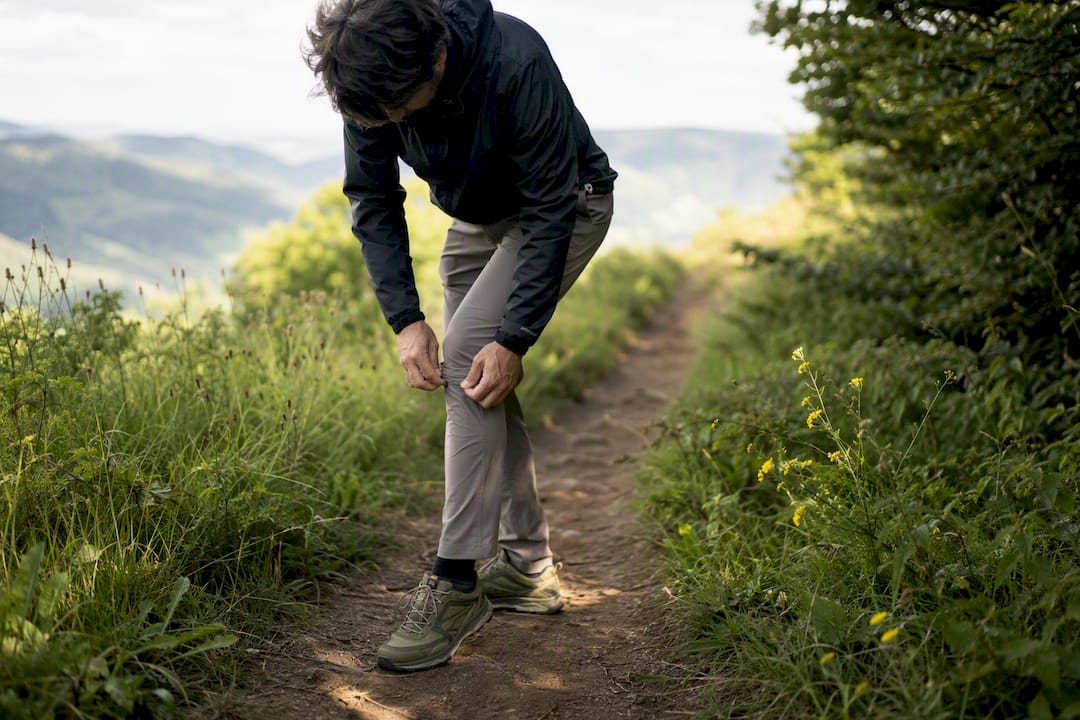 Hiker adjusting stretch pants on trail in trail runners