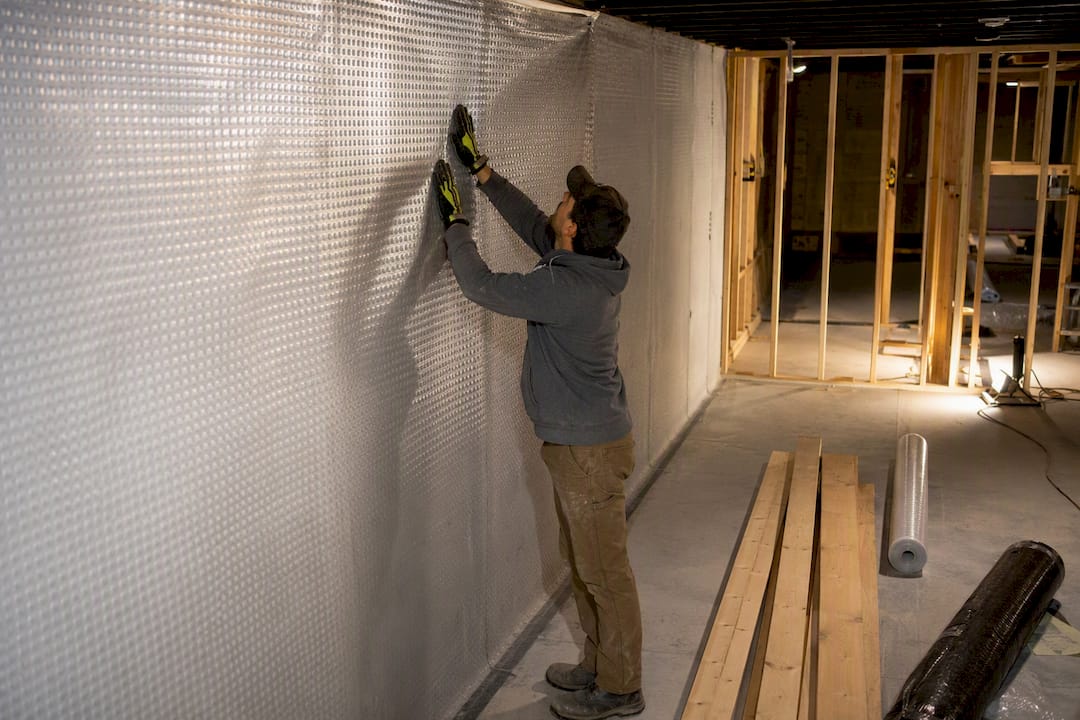 Hands installing vapour barrier in basement wall framing