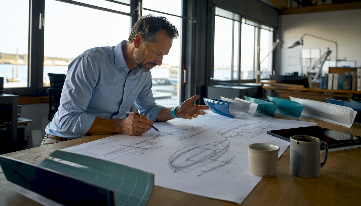 Hands sketching hull form designs on drafting paper