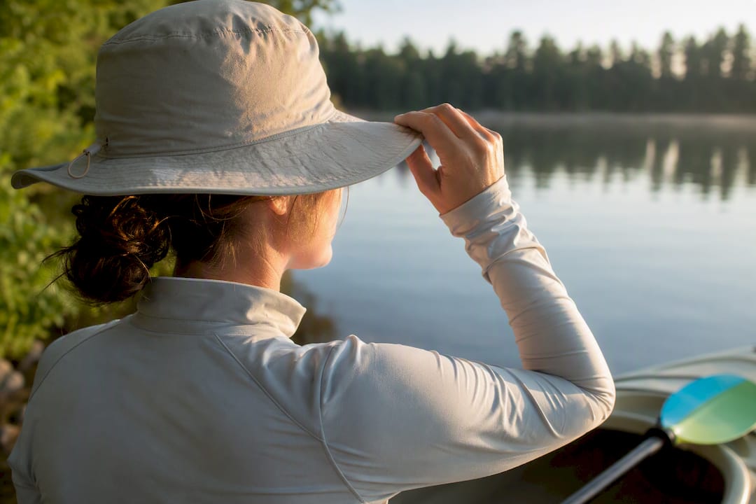 Paddler adjusting hat beside calm lake