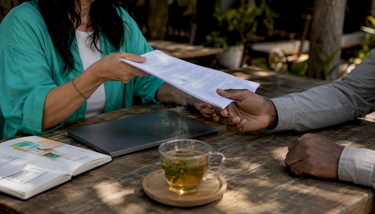 Hands exchanging redlined contract drafts at workspace