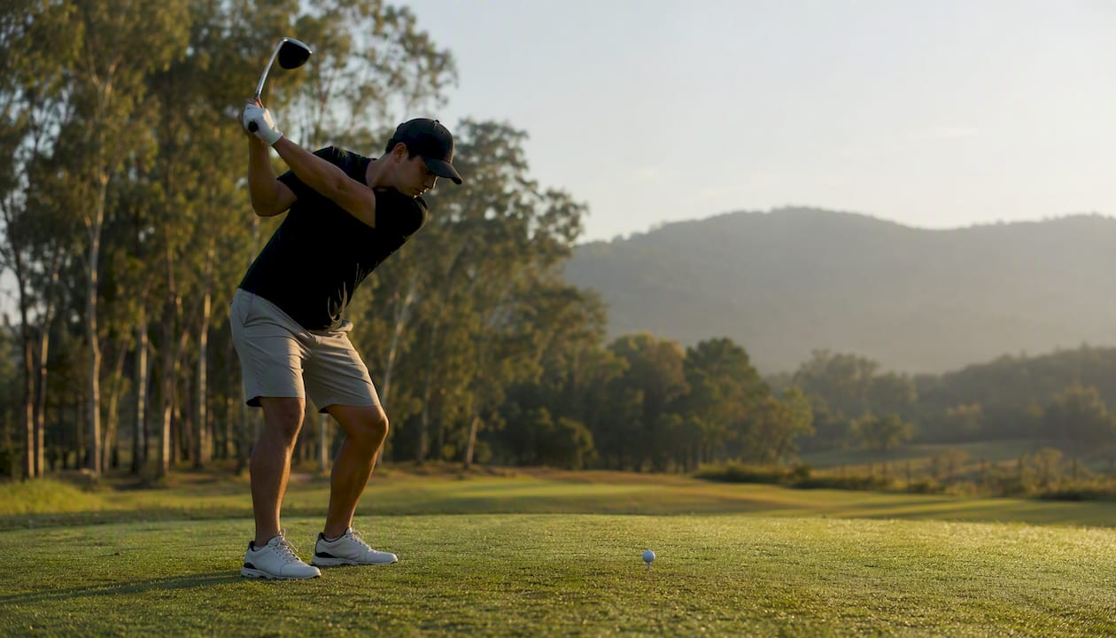 Golfer teeing off in a sunny parkland golf course
