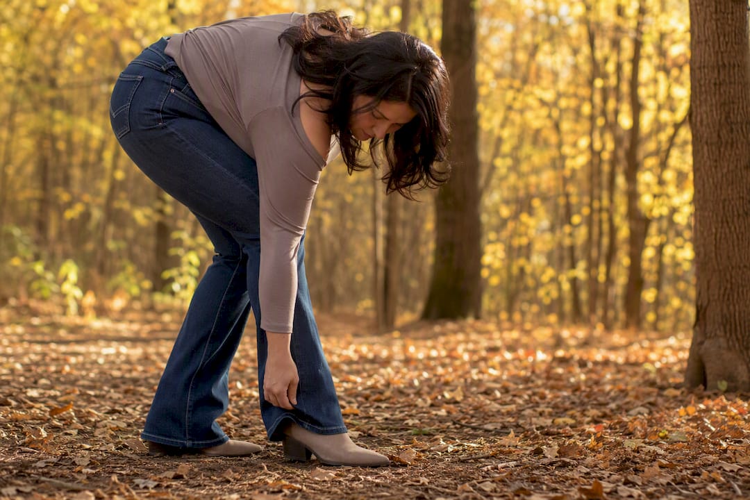 Eine Frau mit birnenförmiger Figur richtet den Schlag ihrer Bootcut-Jeans zurecht.