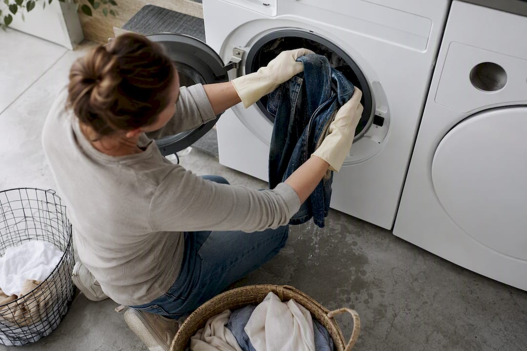 Handen met handschoenen die natte spijkerbroeken uit een bak tillen