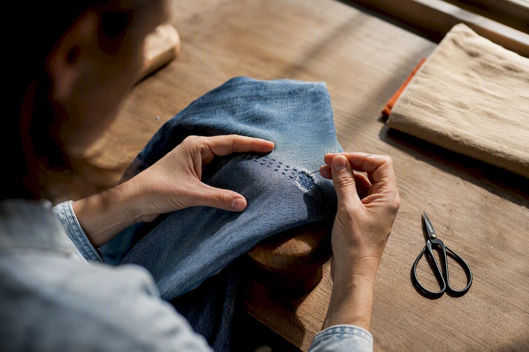 Handen repareren een gescheurde knie van denim