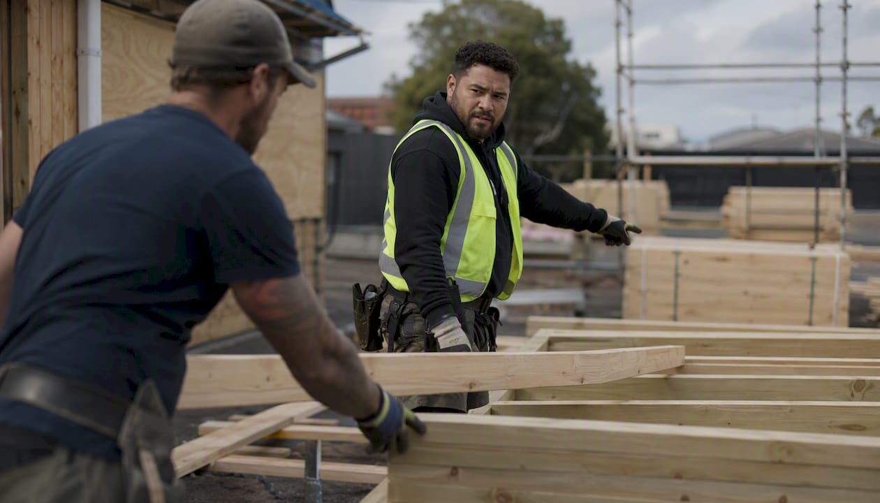 Hands fitting wooden framing beams on construction site
